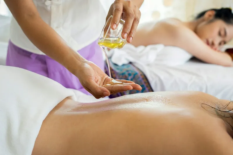 Terapeuta vierte aceite en su mano junto a dos personas recostadas en camillas de masaje
