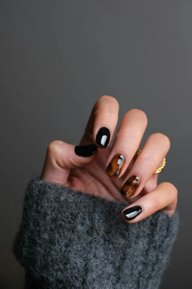 Mano con uñas cortas esmaltadas en negro y carey sobre un suéter gris
