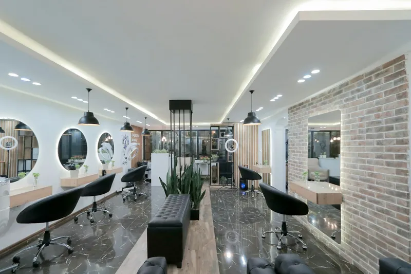 Interior del salón: tocadores con espejos redondos, sillas negras y una pared de ladrillo